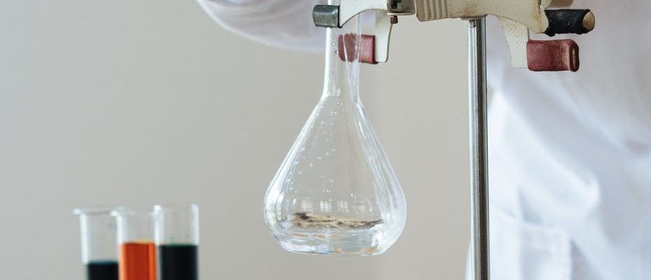 crop chemist pouring clear liquid into fragile glassware in science center